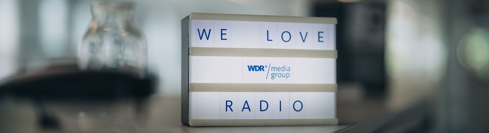 Ein kleiner Leuchtkasten zeigt die Worte WE LOVE RADIO und das Logo der WDR mediagroup. | Bildquelle: WDR mediagroup GmbH Ein kleiner Leuchtkasten zeigt die Worte WE LOVE RADIO und das Logo der WDR mediagroup.
