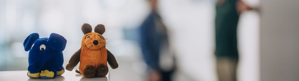 Im Vordergrund sind Die Maus und Der Elefant als Stofftiere zu sehen. Im Hintergrund sieht man zwei Personen, die sich unterhalten. | Bildquelle: WDR mediagroup GmbH Im Vordergrund sind Die Maus und Der Elefant als Stofftiere zu sehen. Im Hintergrund sieht man zwei Personen, die sich unterhalten.